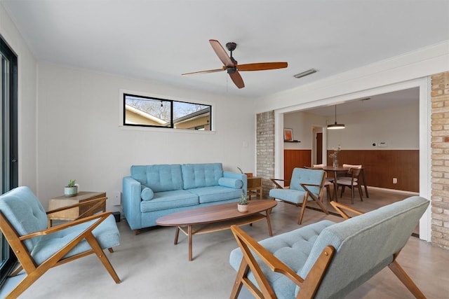 living room featuring visible vents, concrete floors, ceiling fan, and a wainscoted wall