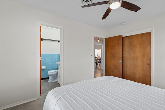 bedroom with ensuite bath, ceiling fan, a closet, concrete flooring, and tile walls