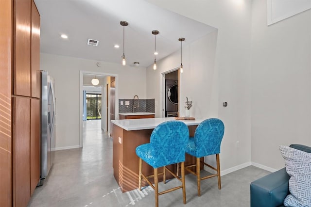 kitchen featuring visible vents, concrete floors, stainless steel fridge with ice dispenser, stacked washing maching and dryer, and brown cabinetry