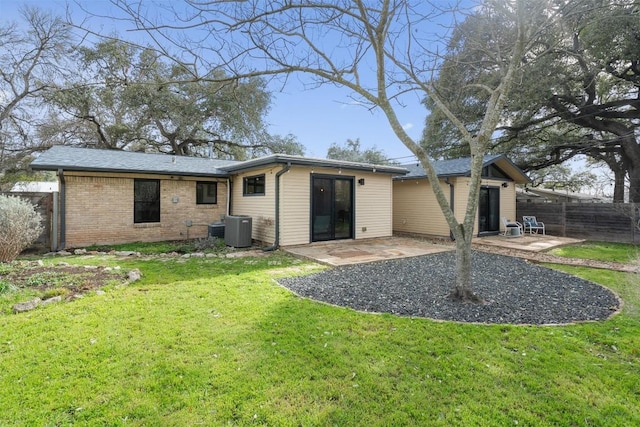 back of property featuring fence, a yard, brick siding, central AC unit, and a patio area