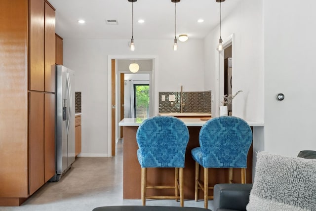 4810 Enchanted Ln, Austin, TX 78745 - kitchen with stainless steel fridge, concrete flooring, decorative light fixtures, light countertops, and brown cabinets