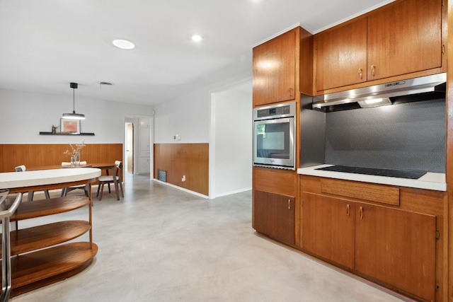 4810 Enchanted Ln, Austin, TX 78745 - kitchen featuring oven, under cabinet range hood, black electric cooktop, brown cabinetry, and a wainscoted wall