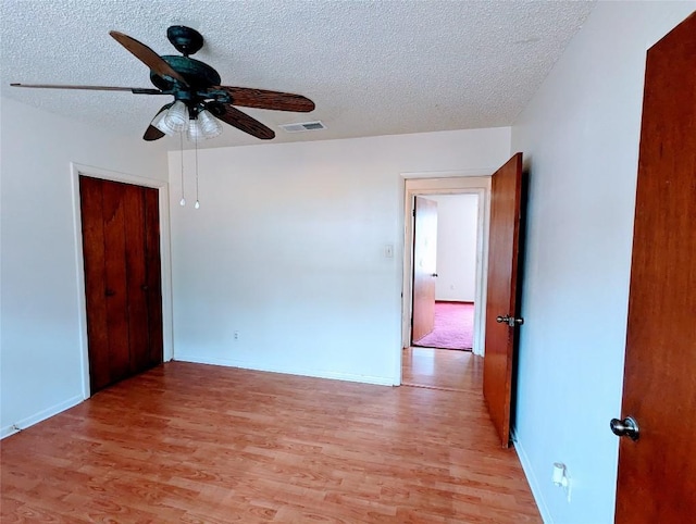 spare room featuring light wood finished floors, visible vents, a ceiling fan, a textured ceiling, and baseboards