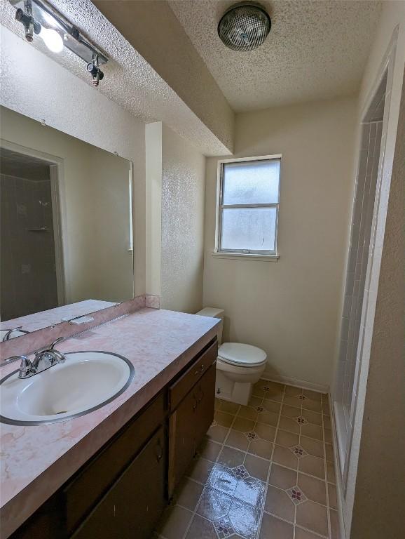 bathroom with a textured ceiling, a textured wall, tile patterned flooring, toilet, and vanity