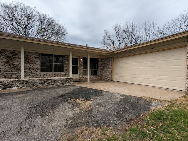 ranch-style house with an attached garage, stone siding, and aphalt driveway