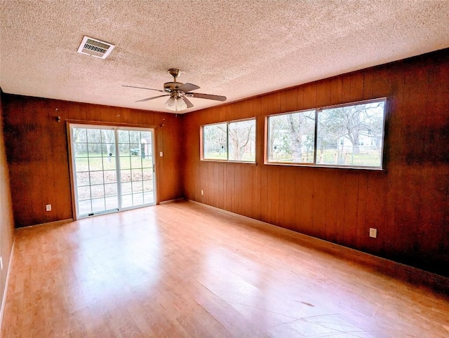 spare room with light wood-type flooring, ceiling fan, visible vents, and a textured ceiling