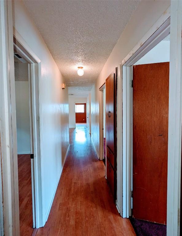 hall with a textured ceiling, wood finished floors, and baseboards