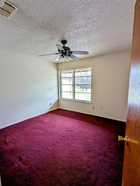 unfurnished room featuring a textured ceiling, a ceiling fan, visible vents, baseboards, and dark colored carpet