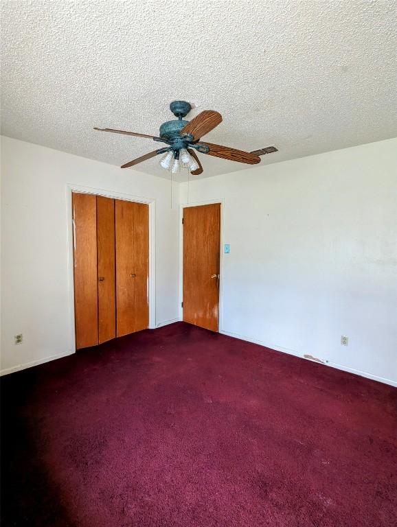 unfurnished bedroom featuring a textured ceiling, dark colored carpet, a closet, and visible vents