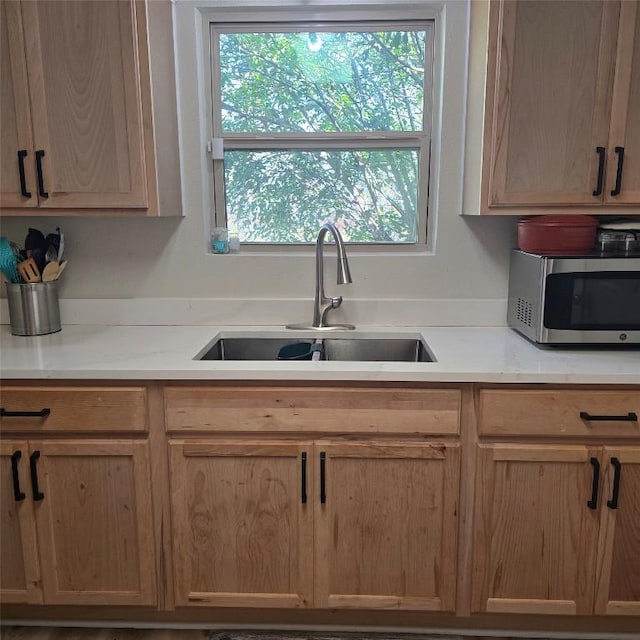 kitchen with light countertops, stainless steel microwave, a sink, and light brown cabinetry