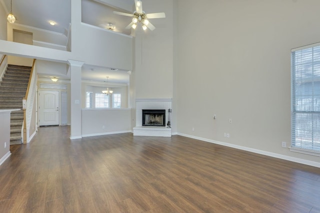 unfurnished living room with stairs, dark wood finished floors, a fireplace, baseboards, and ceiling fan with notable chandelier