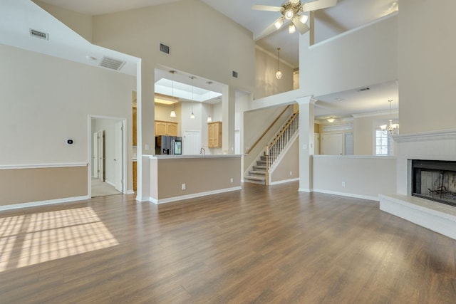 unfurnished living room with ceiling fan with notable chandelier, a brick fireplace, wood finished floors, and visible vents