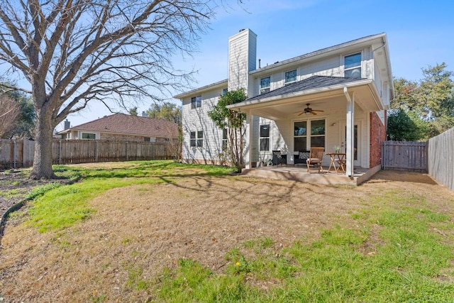 rear view of property with a ceiling fan, a yard, a fenced backyard, a chimney, and a patio area