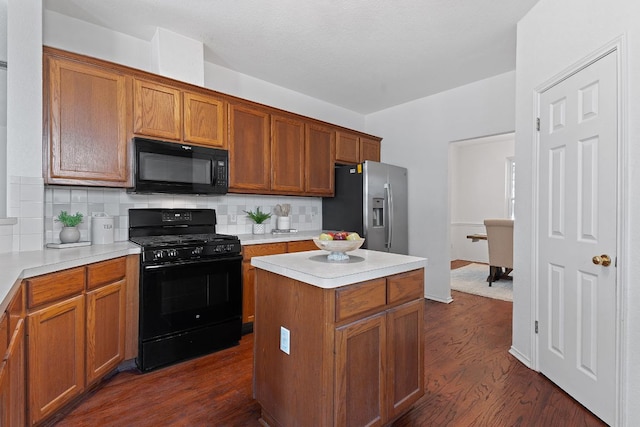 kitchen with dark wood-style floors, a kitchen island, black appliances, light countertops, and backsplash