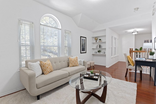 living room with dark wood-type flooring, built in shelves, baseboards, and lofted ceiling