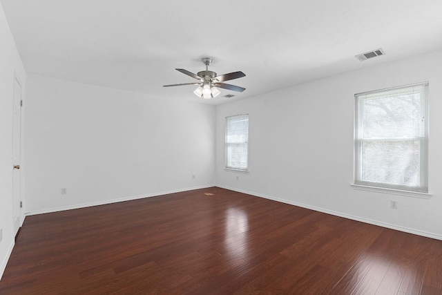 spare room with dark wood-type flooring, baseboards, visible vents, and ceiling fan