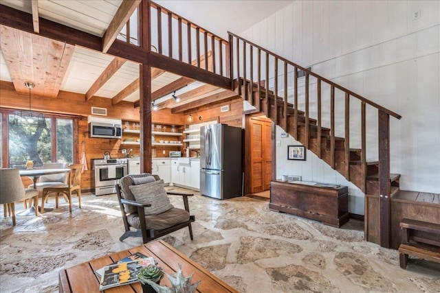 living room with stone flooring, beam ceiling, wooden walls, and stairs