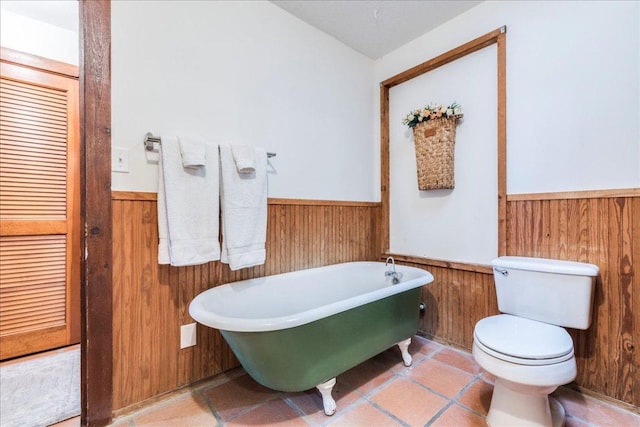 full bath with toilet, wood walls, a freestanding tub, and wainscoting