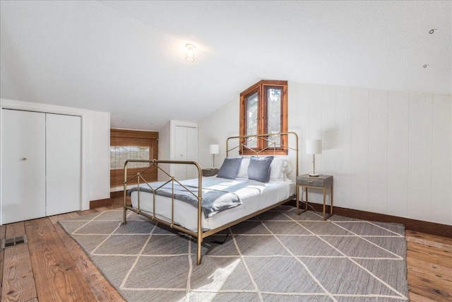 bedroom with lofted ceiling, hardwood / wood-style floors, visible vents, and baseboards