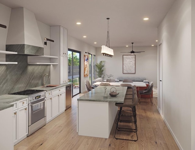 kitchen with appliances with stainless steel finishes, open floor plan, wall chimney range hood, open shelves, and a sink