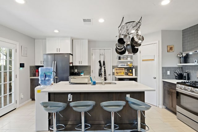 kitchen featuring a center island with sink, appliances with stainless steel finishes, a breakfast bar area, light countertops, and decorative backsplash