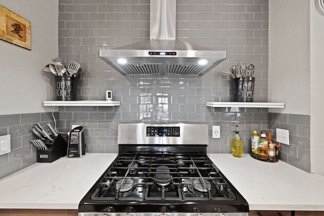 kitchen with stainless steel gas range oven, range hood, light stone countertops, and open shelves