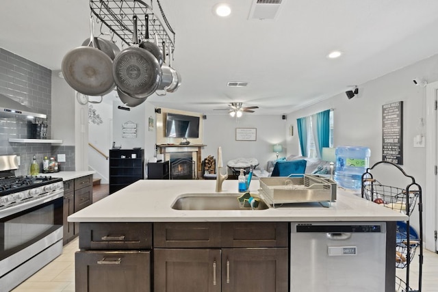 kitchen with visible vents, a sink, open floor plan, stainless steel appliances, and a lit fireplace