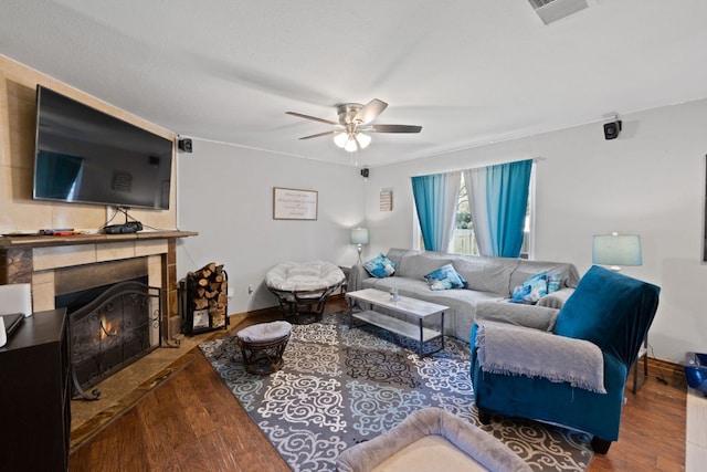 living area featuring a ceiling fan, wood finished floors, visible vents, baseboards, and a fireplace with flush hearth