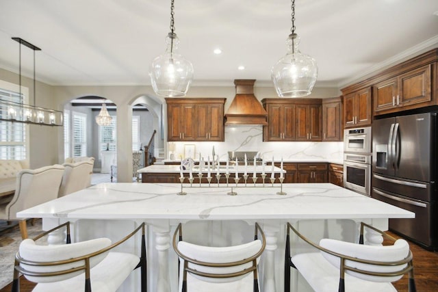 kitchen featuring a large island, backsplash, stainless steel appliances, arched walkways, and custom exhaust hood