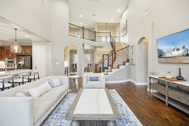 living room with arched walkways, visible vents, dark wood finished floors, and stairs