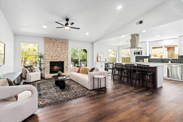 living area featuring ceiling fan, a stone fireplace, dark wood-style floors, vaulted ceiling, and recessed lighting