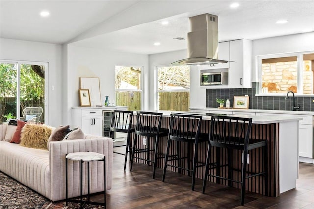 kitchen with island exhaust hood, stainless steel microwave, a sink, a center island, and white cabinets