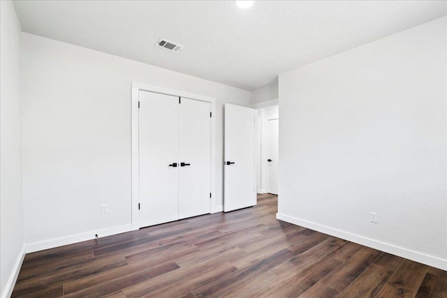 unfurnished bedroom with a closet, wood finished floors, visible vents, and baseboards