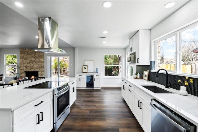 kitchen with visible vents, wall chimney exhaust hood, wine cooler, appliances with stainless steel finishes, and a sink