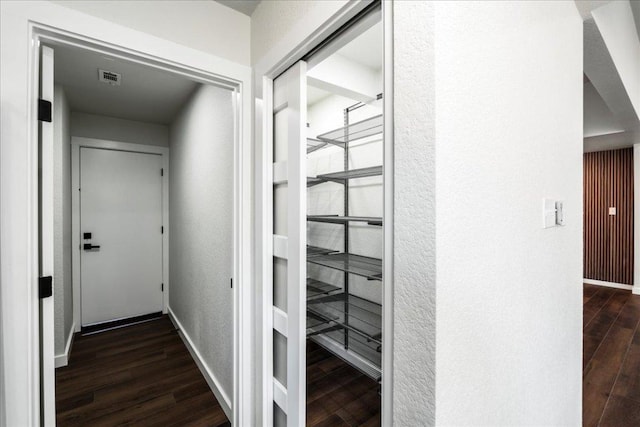 hallway featuring dark wood-style floors, a textured wall, visible vents, and baseboards