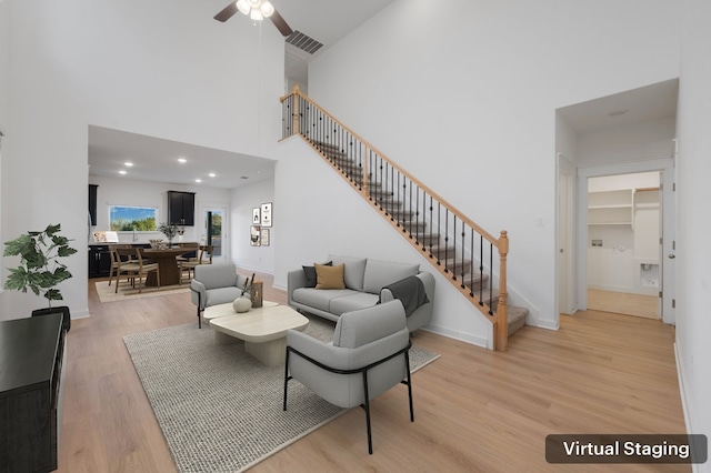 living room featuring light wood finished floors, baseboards, visible vents, stairway, and a high ceiling