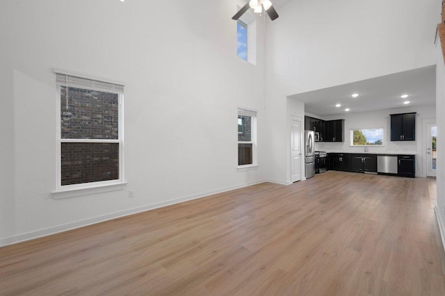 unfurnished living room with light wood-type flooring, a high ceiling, ceiling fan, and baseboards