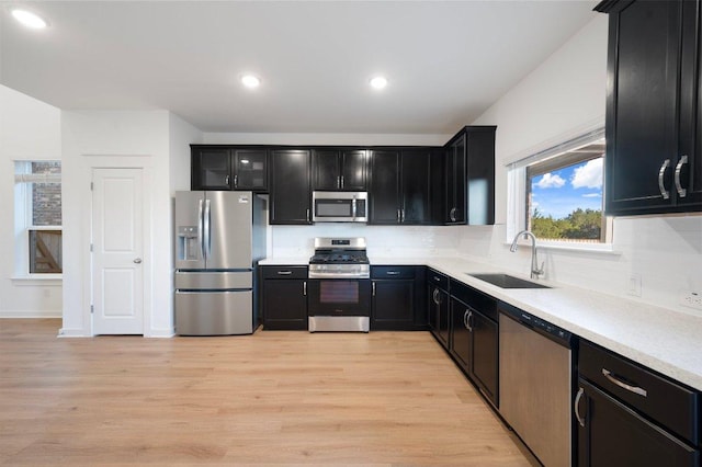 kitchen featuring tasteful backsplash, dark cabinets, stainless steel appliances, light wood-type flooring, and a sink