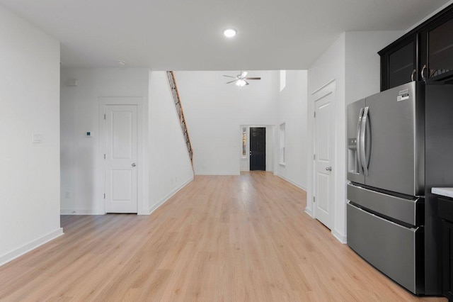 kitchen featuring stainless steel fridge with ice dispenser, light wood-style flooring, ceiling fan, dark cabinetry, and baseboards