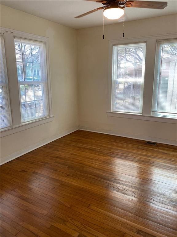 empty room with a ceiling fan, a wealth of natural light, visible vents, and wood finished floors