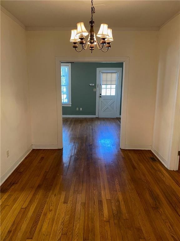 unfurnished dining area featuring an inviting chandelier, crown molding, baseboards, and dark wood-type flooring