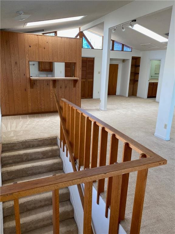 staircase featuring lofted ceiling, wood walls, carpet, and rail lighting