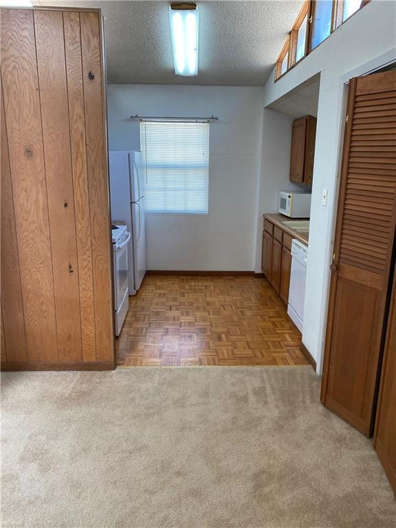 kitchen featuring white appliances, brown cabinets, a textured ceiling, and baseboards