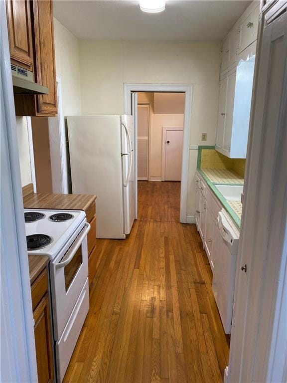 kitchen featuring under cabinet range hood, white appliances, light countertops, light wood-type flooring, and brown cabinetry