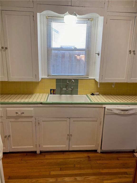 kitchen featuring wood finished floors, white dishwasher, a sink, and white cabinets