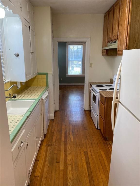 kitchen featuring white cabinetry, a sink, wood finished floors, white appliances, and under cabinet range hood