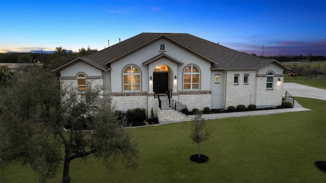 view of front of property featuring a yard, a shingled roof, stone siding, and stucco siding