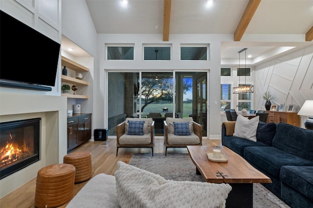 living area with built in features, light wood finished floors, beamed ceiling, a glass covered fireplace, and an inviting chandelier