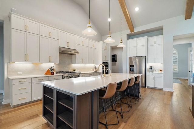 kitchen with light countertops, appliances with stainless steel finishes, white cabinets, a sink, and under cabinet range hood