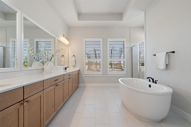 full bath with a sink, a freestanding bath, a tray ceiling, and a wealth of natural light